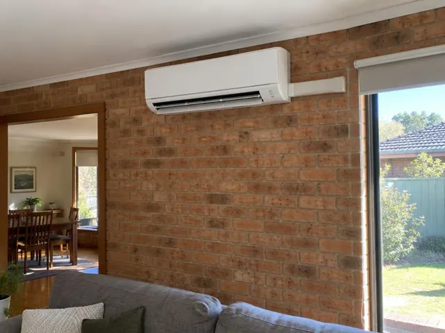 White split-system indoor unit mounted high on a brick wall in a lived-in home interior in Redwood Park