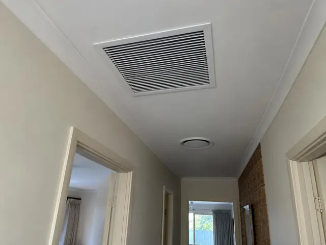 Ceiling return-air grille and round outlet in a narrow hallway with doorways and brick wall in Wynn Vale